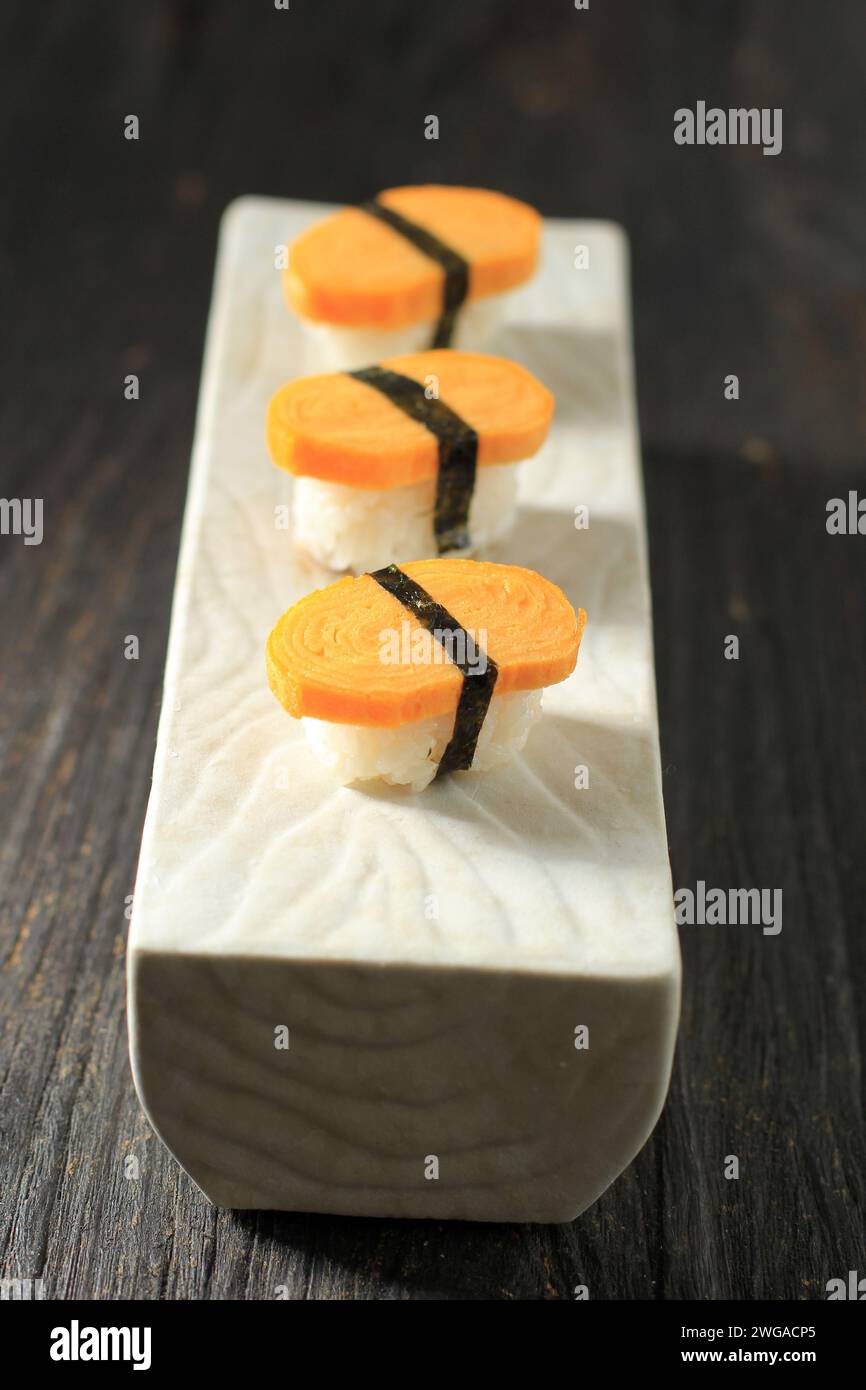 Tre Tamago Nigiri Egg Sushi con Nori su tavolo di legno, riso con uova arrotolate e Nori Belt Foto Stock