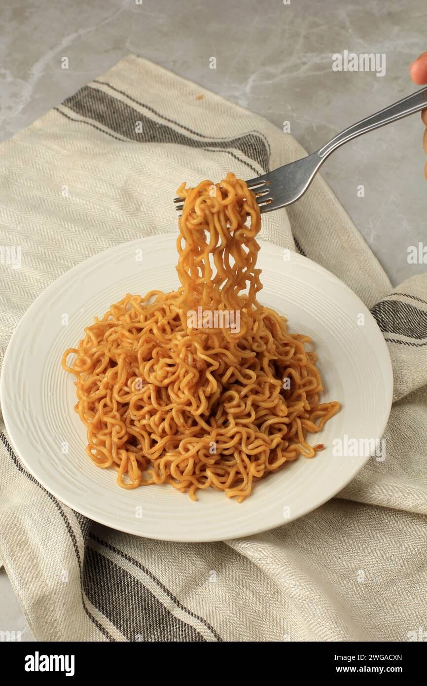 Mangia gli spaghetti fritti Indomie Goreng, prendi gli spaghetti con la forchetta. Su piastra bianca Foto Stock