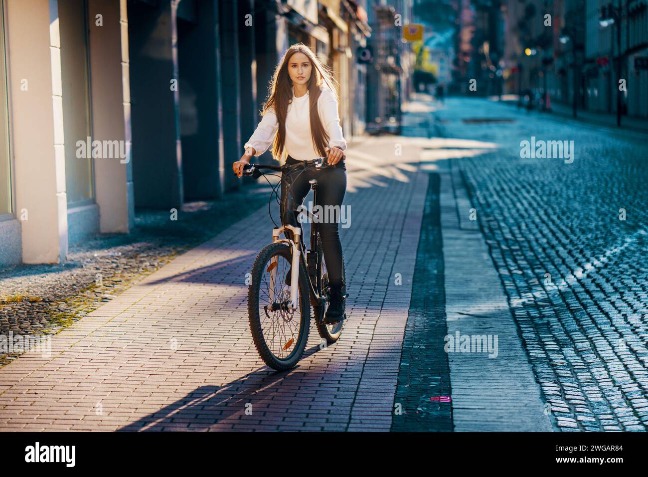 Giovane donna in bicicletta per le strade della città con un grande sorriso Foto Stock
