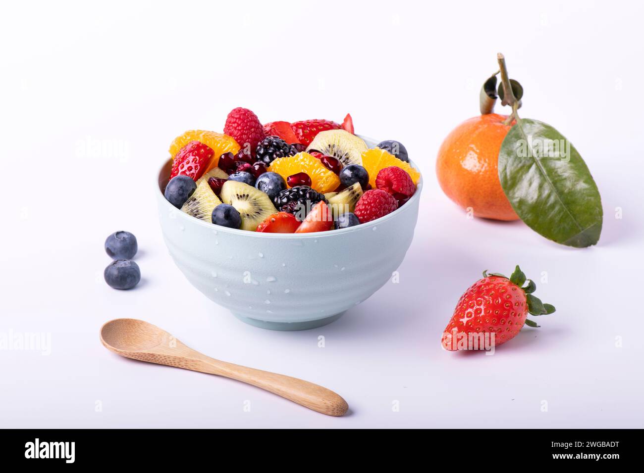 Macedonia di frutta fresca mista in un recipiente con un cucchiaio di legno in primo piano. Sfondo bianco Foto Stock