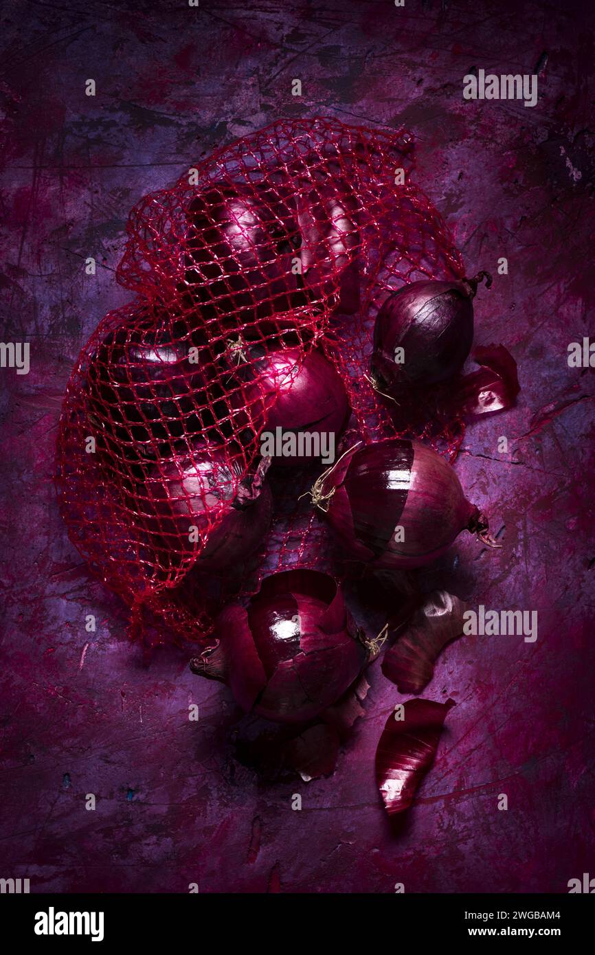 Cipolle rosse nella retina su sfondo scuro con sfumature di rosso e viola, vista dall'alto. Natura morta Foto Stock