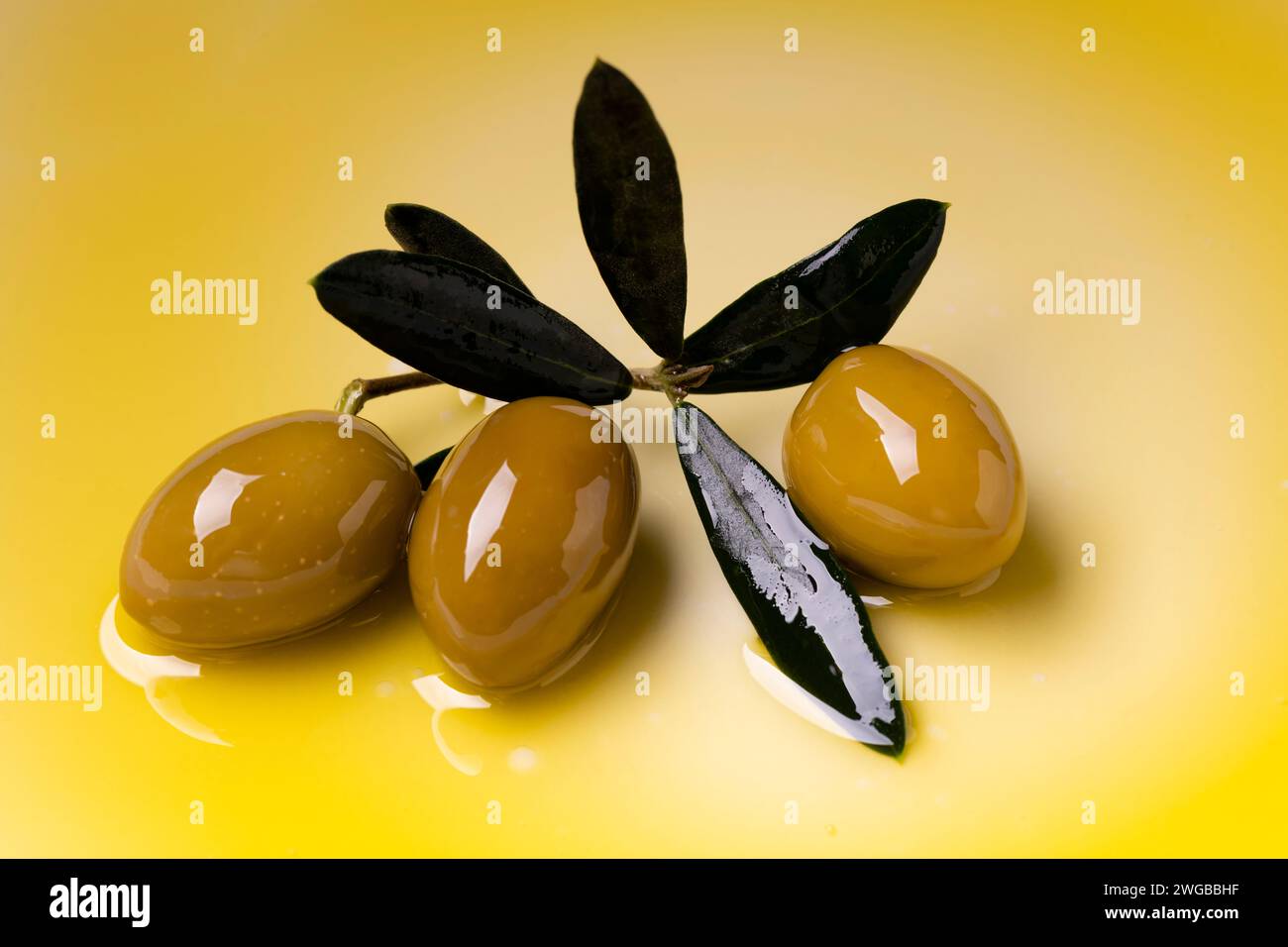 in primo piano 3 olive verdi e alcune foglie di oliva poste su uno strato di olio extra vergine di oliva Foto Stock