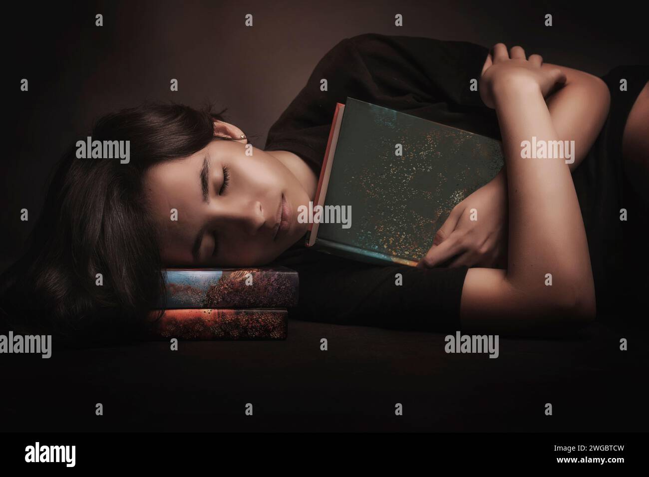 Adolescente che abbraccia un libro mentre riposa la testa su una pila di libri cartacei Foto Stock