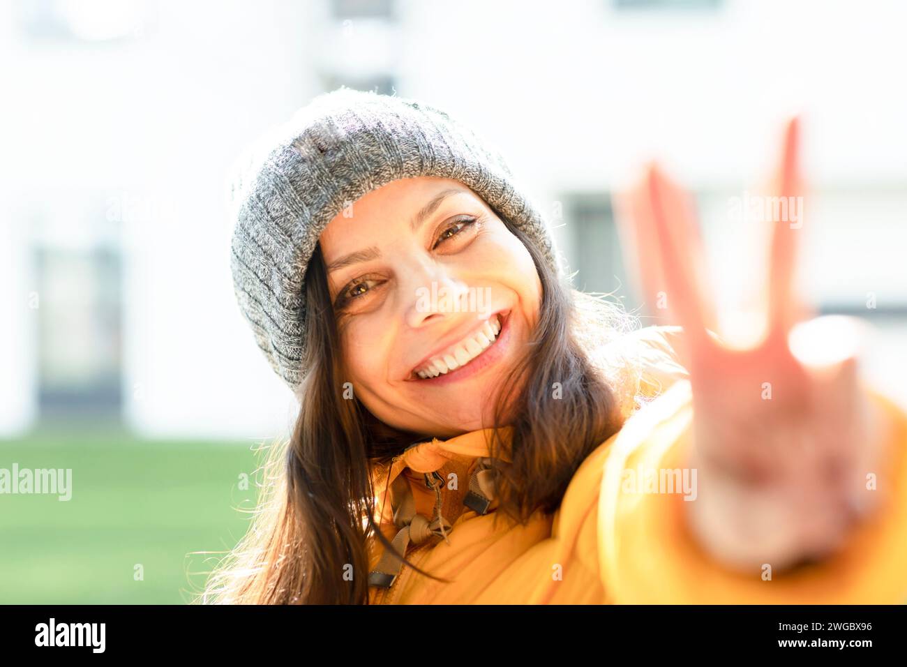 Ritratto di una donna sorridente in piedi di fronte a un quartiere residenziale con abiti caldi che fanno un segno di pace con la mano, la Germania Foto Stock