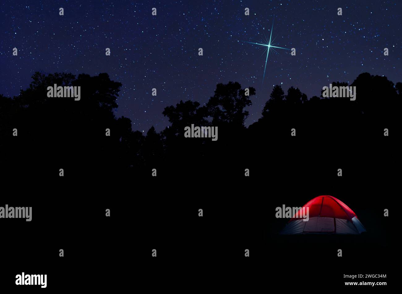 Stella del Natale sopra una tenda rossa con zaino in spalla, immersa in una foresta scura e impreziosita da un luminoso cielo stary alle spalle. Foto Stock