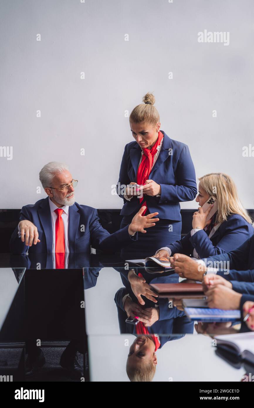 Due segretari biondi di mezza età discutono con il proprietario della loro azienda durante la riunione nella moderna sala conferenze Foto Stock