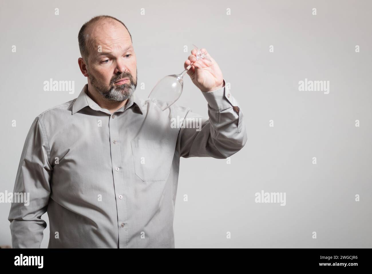 Uomo caucasico che guarda un bicchiere di vino vuoto, sfondo bianco. Immagine concettuale della Dry Challenge Foto Stock
