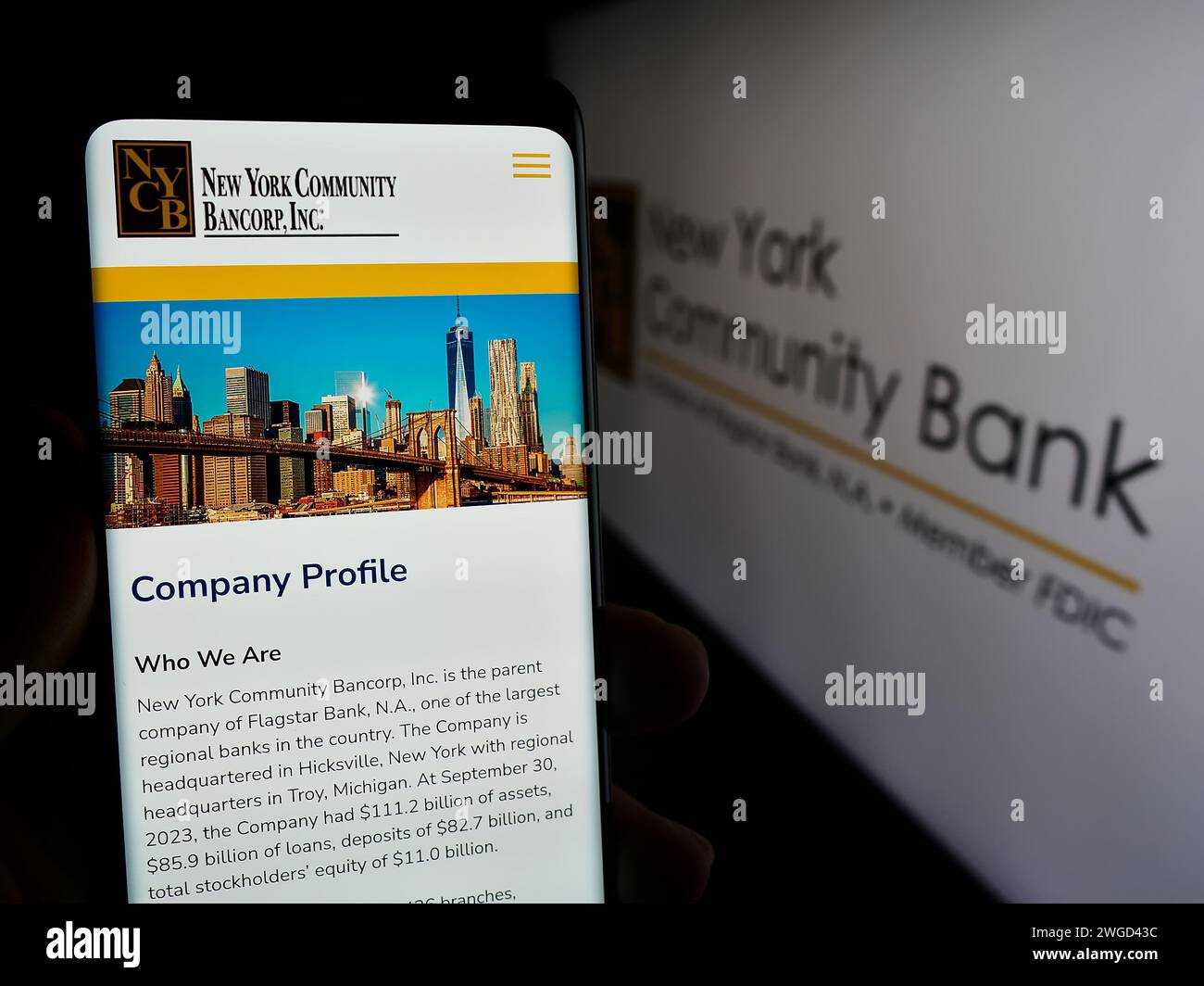 Persona che possiede uno smartphone con pagina Web della società statunitense New York Community Bancorp Inc (NYCB) di fronte al logo. Messa a fuoco al centro del display del telefono. Foto Stock