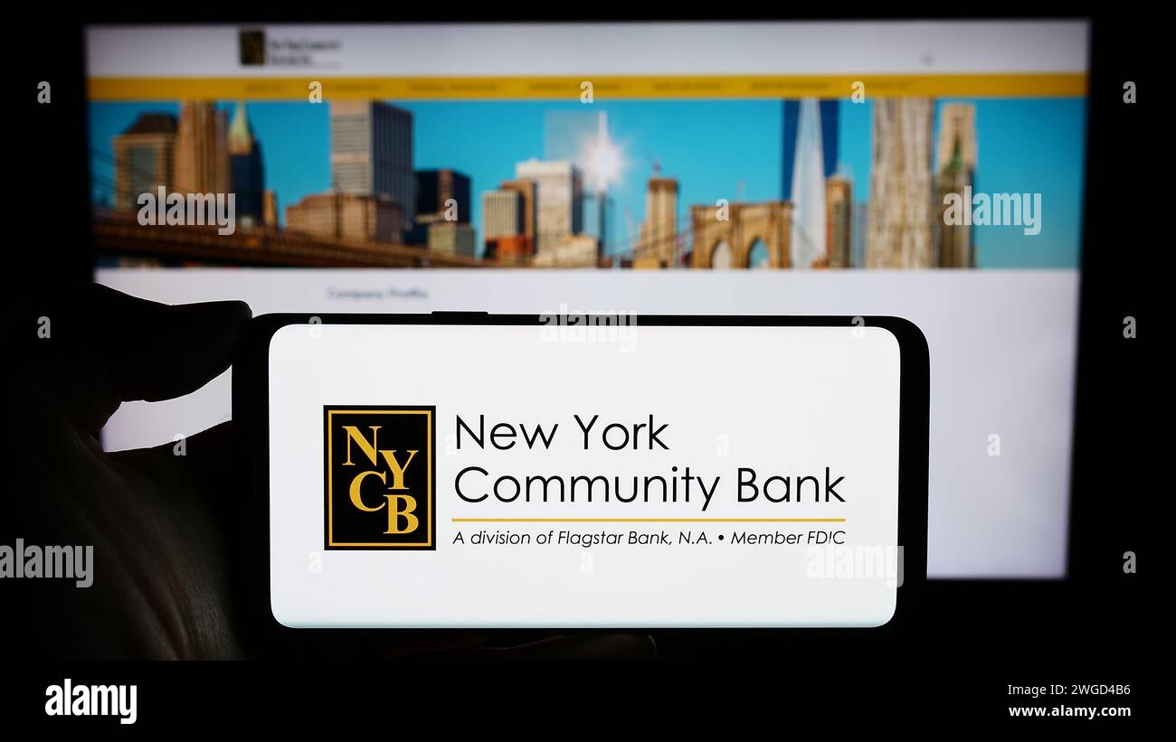 Persona che detiene un cellulare con il logo della società statunitense New York Community Bancorp Inc (NYCB) di fronte alla pagina Web aziendale. Mettere a fuoco il display del telefono. Foto Stock