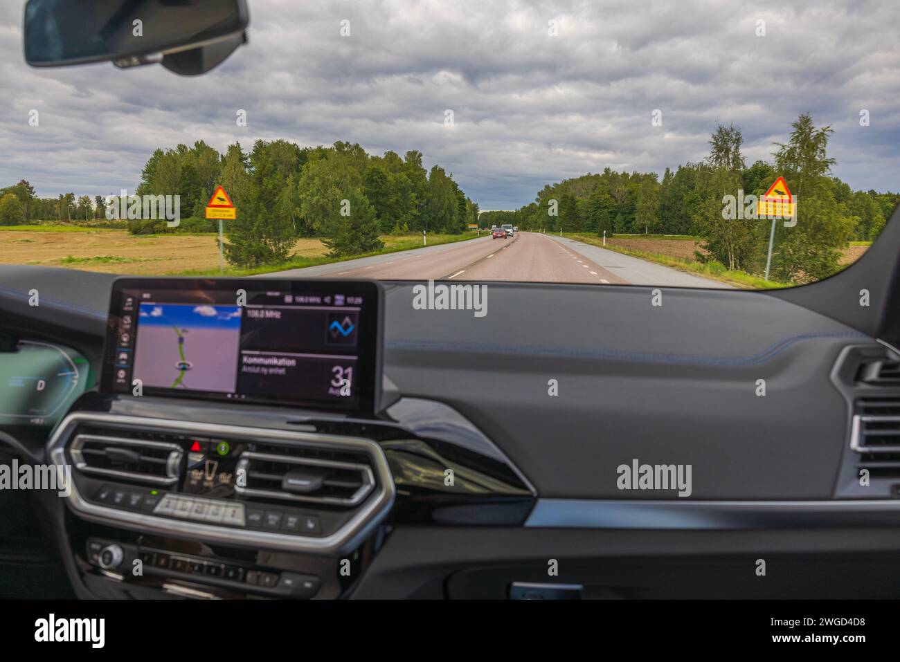 Splendida vista dal parabrezza anteriore dell'auto elettrica BMW iX3 M Sport sul paesaggio estivo durante la guida in autostrada. Svezia. Foto Stock