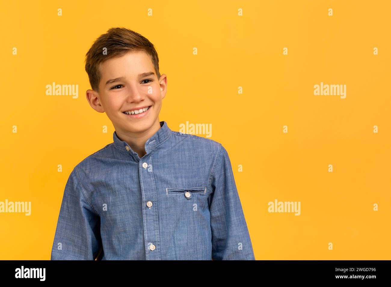 Adolescente felice in camicia in denim che posa con sicurezza su sfondo giallo in studio Foto Stock