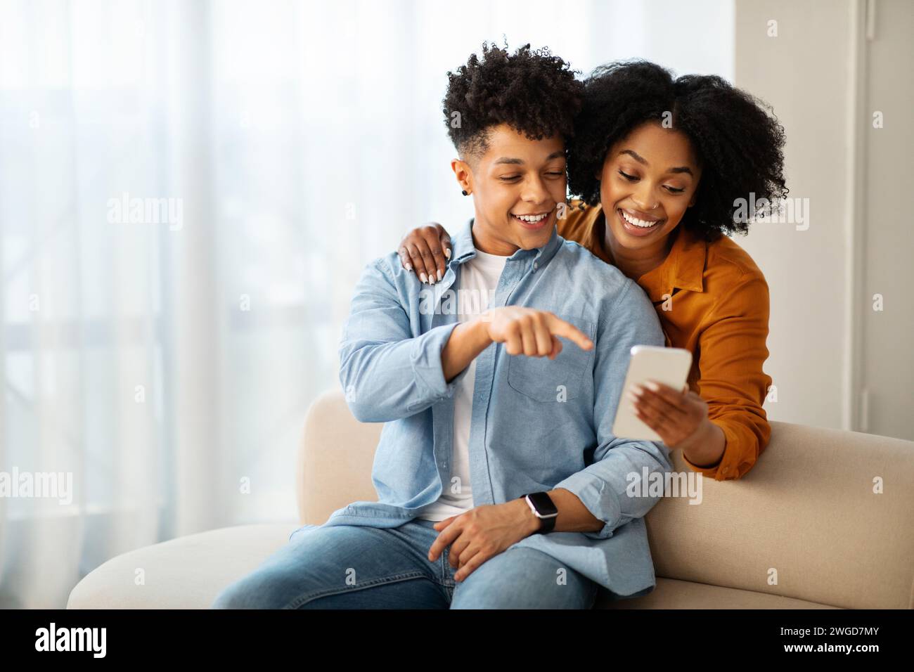Un giovane uomo con una camicia in denim e una donna con un top di senape sono seduti su un divano Foto Stock