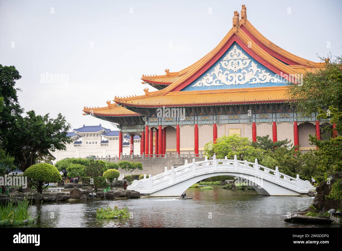 Bellissimo giardino asiatico con bonsais, laghetto con ponte e maestoso tempio sullo sfondo, Taiwan Foto Stock