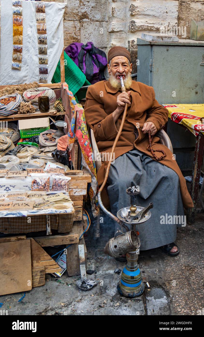 Uomo egiziano che vende spezie al mercato medievale del Cairo con le sue perline di preghiera e fuma un shisha Foto Stock