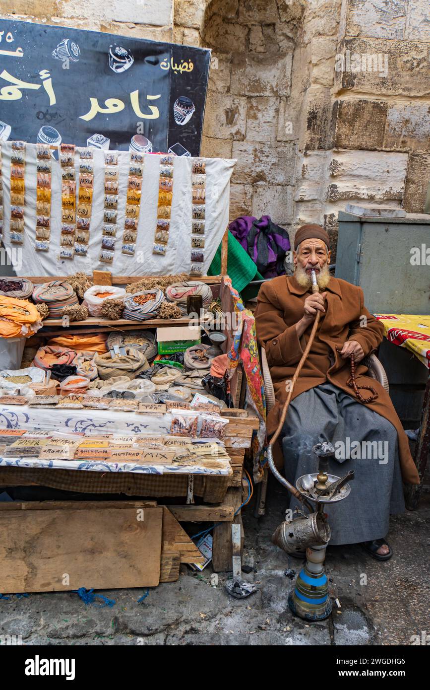 Uomo egiziano che vende spezie al mercato medievale del Cairo con le sue perline di preghiera e fuma un shisha Foto Stock