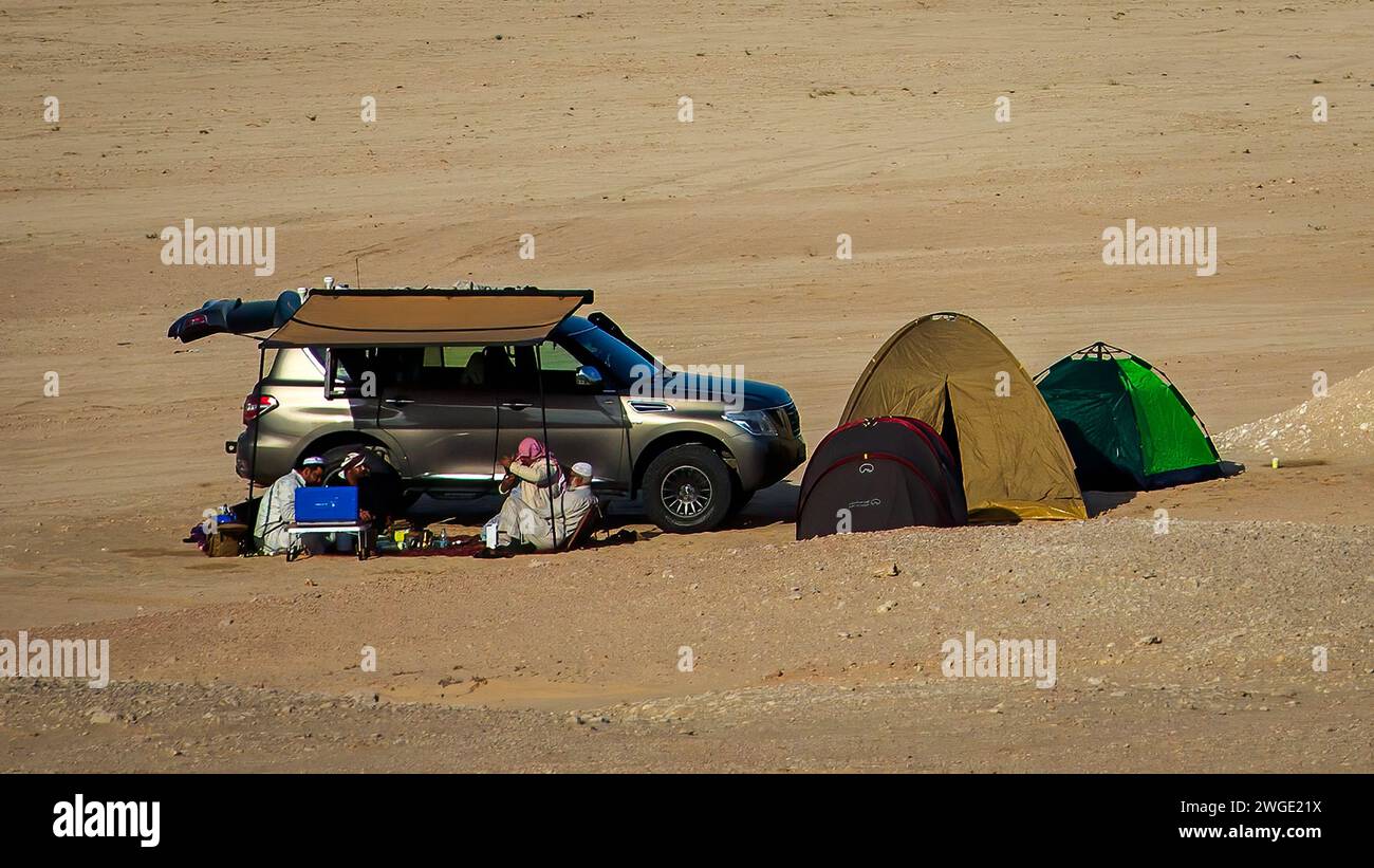 Un piccolo gruppo di persone che si rilassano nel caldo del deserto vicino alla sua auto, in una tenda, vicino a Dhahran, Arabia Saudita. Foto Stock
