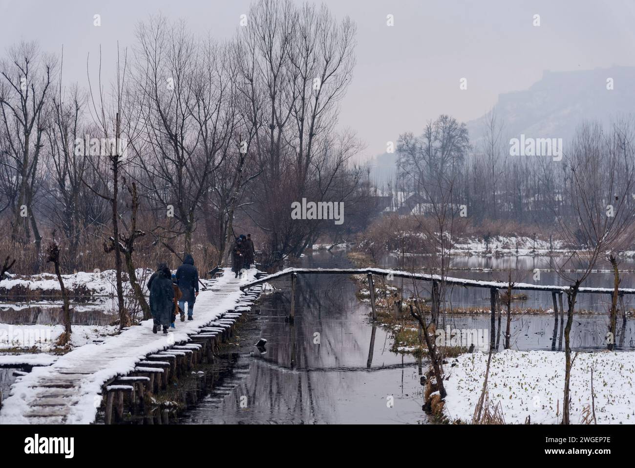 Le persone camminano su un ponte innevato durante le nevicate. Le pianure del Kashmir stanno assistendo a una moderata nevicata, mentre nei tratti più alti della valle sono state segnalate forti nevicate. La valle del Kashmir ha subito una nevicata fresca che ha sconvolto la normale vita delle persone. Le operazioni di volo, il trasporto di superficie e le attività di routine della vita si arrestarono. Foto Stock