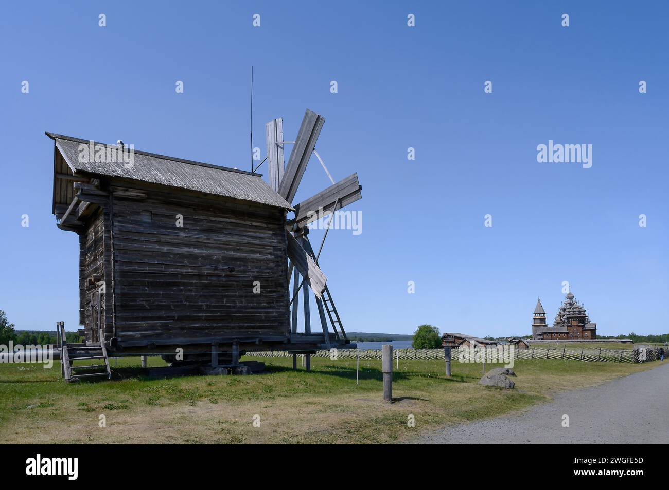 Vista di un mulino a vento in legno con una chiesa medievale della Trasfigurazione all'orizzonte sull'isola di Kizhi in Carelia Foto Stock