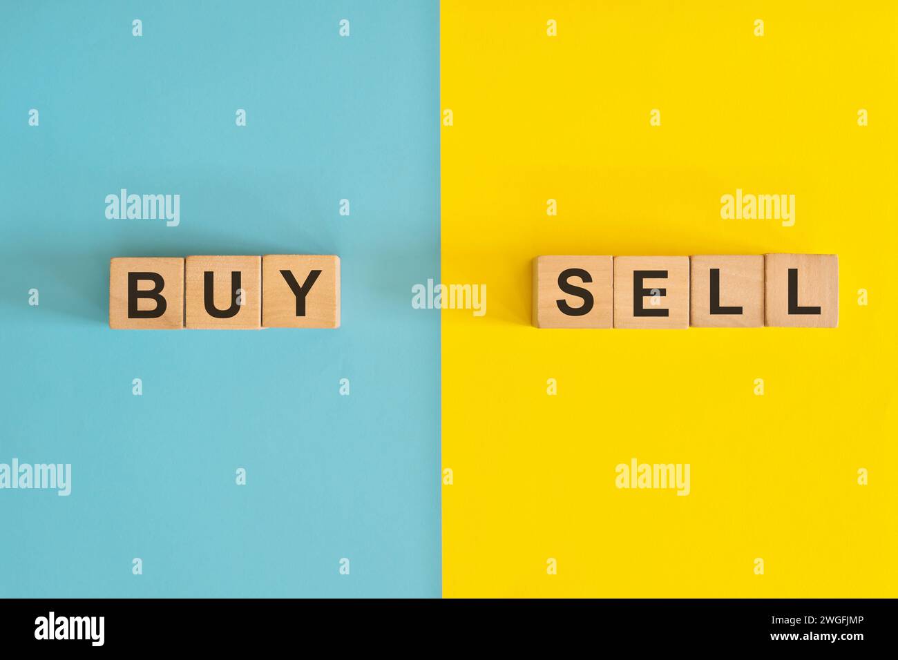 Compra e vendi nel business e nel concetto di investimento. Tipografia con blocchi di legno su sfondo blu e giallo. Foto Stock