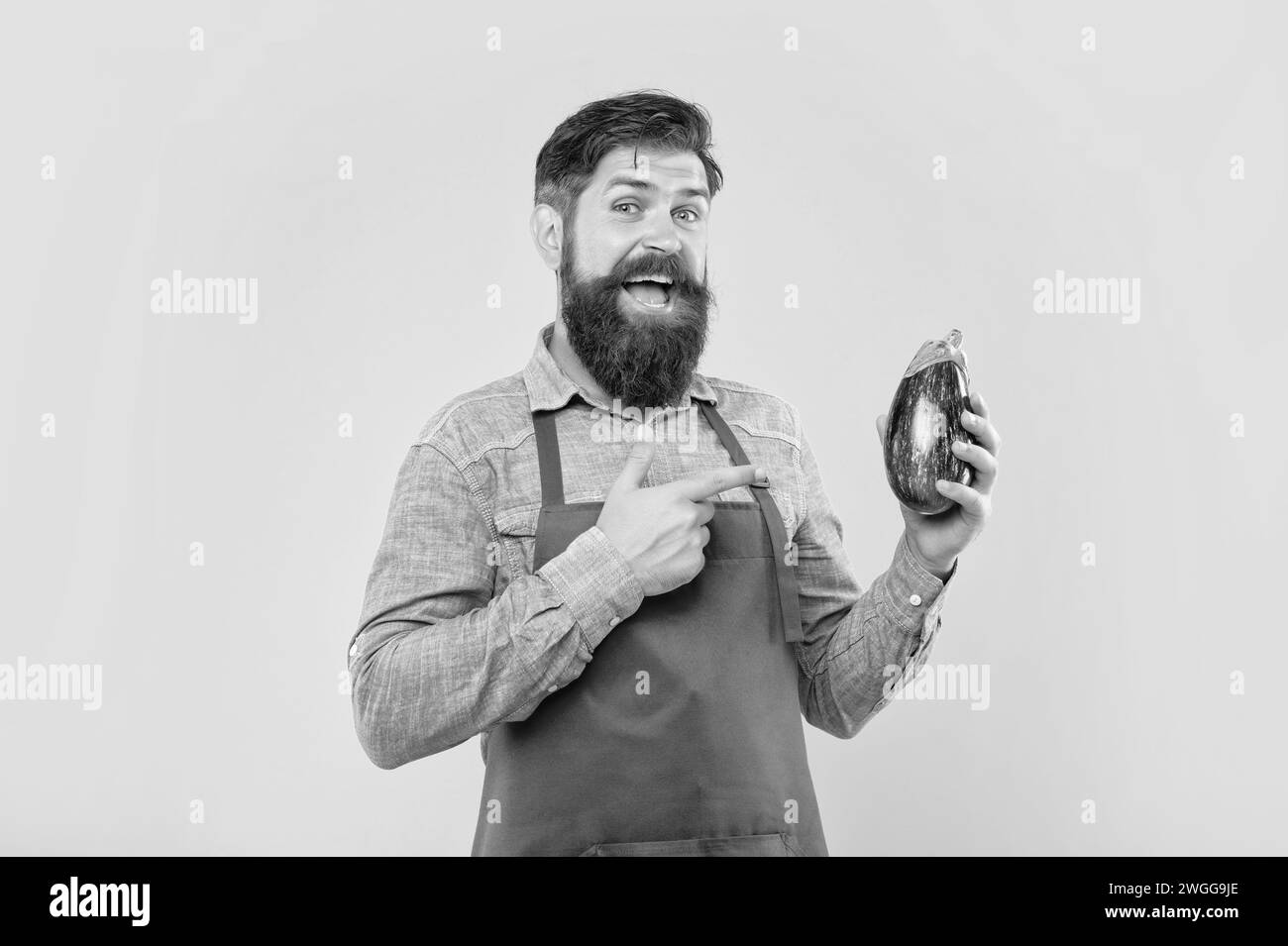 Uomo felice in grembiule rosso puntando il dito su sfondo giallo melanzana, negoziante Foto Stock