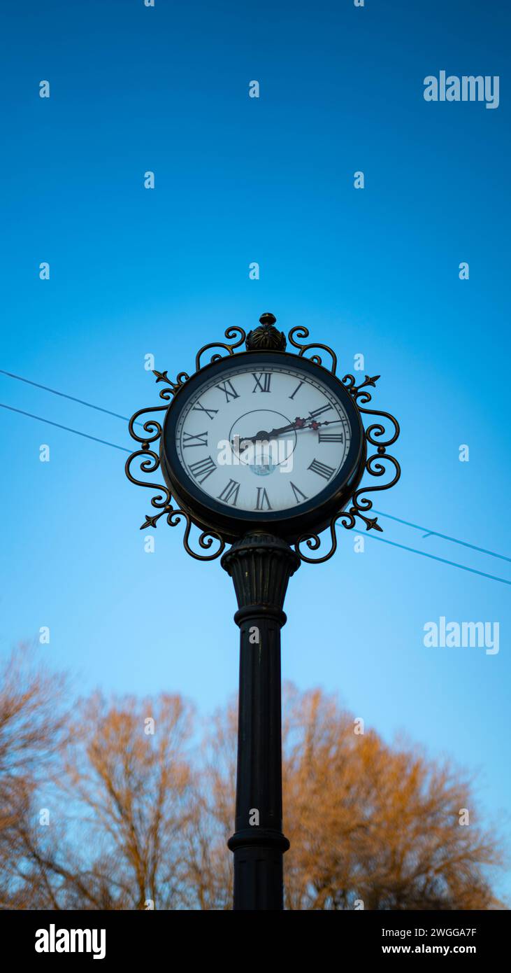 Un antico orologio cittadino nero con un cielo blu sullo sfondo. Foto Stock