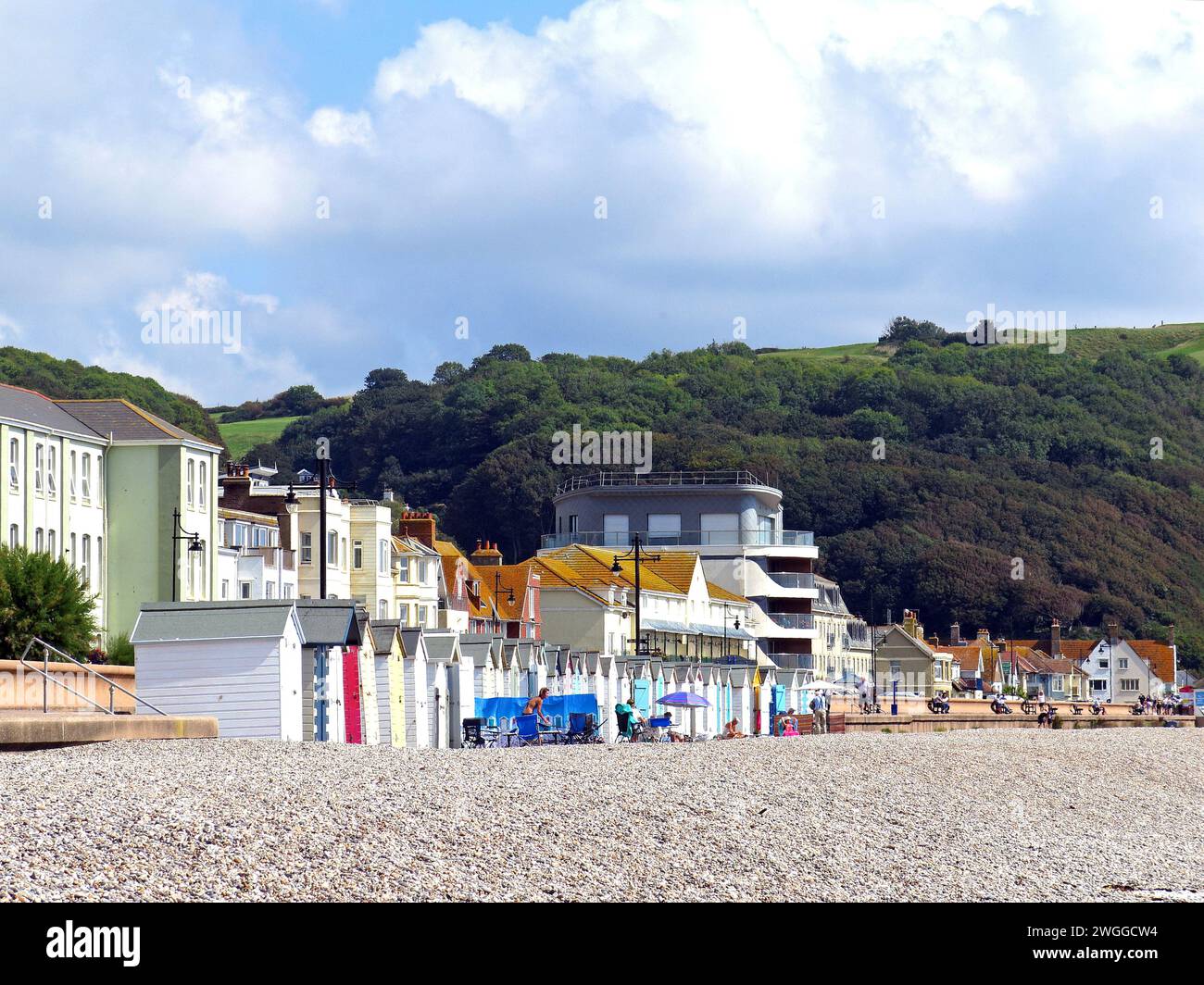 Turisti e capanne lungo la spiaggia con edifici cittadini sul retro, Seaton, Devon, UK, Europa. Foto Stock