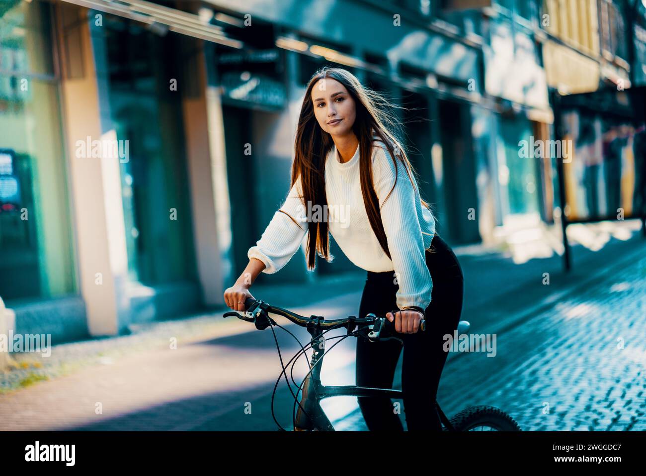 Una giovane donna sorridente in bicicletta per le strade della città con abbigliamento casual Foto Stock