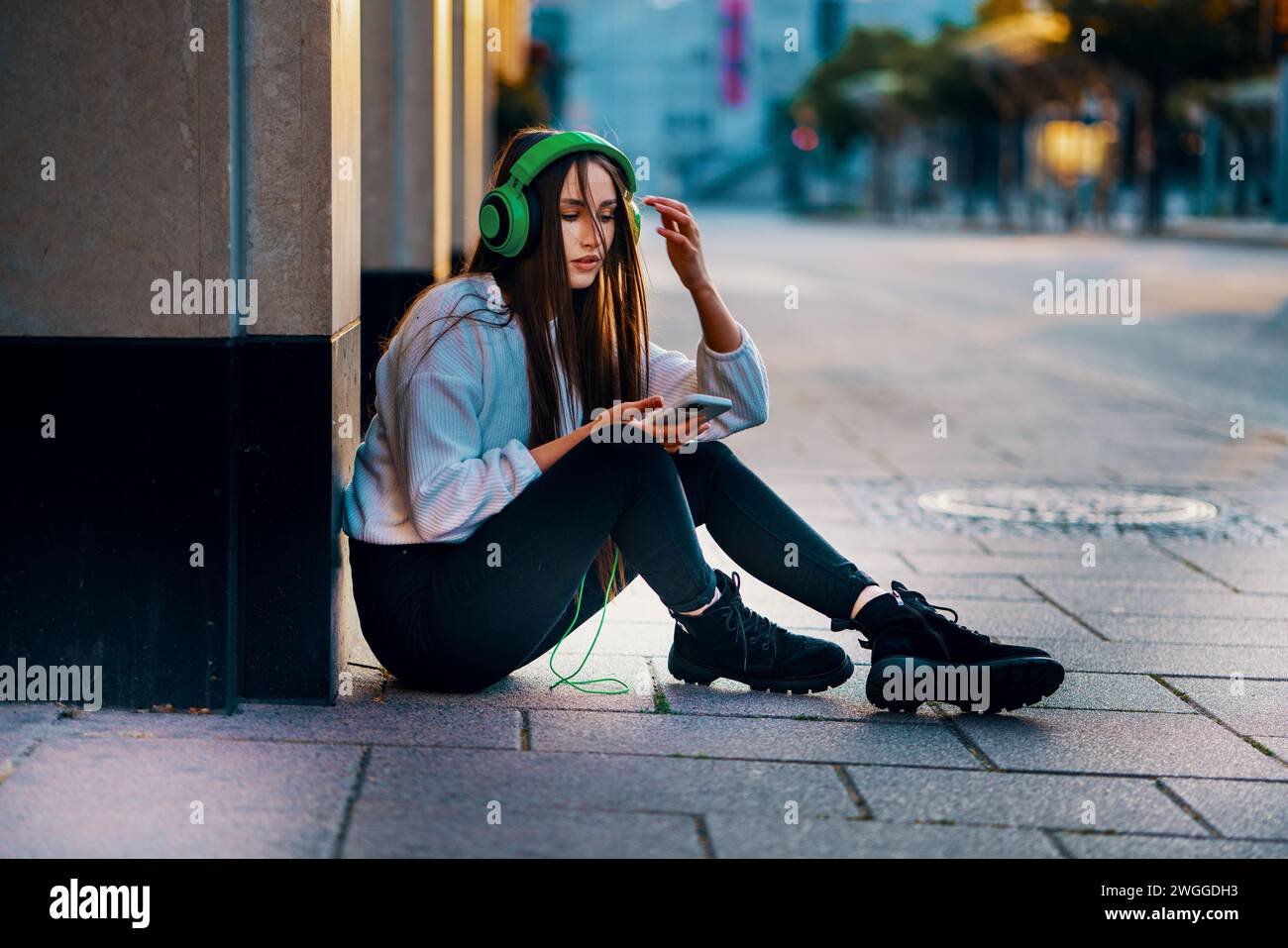 Rilassata giovane donna seduta su City Street, godendo della vita informale della città Foto Stock