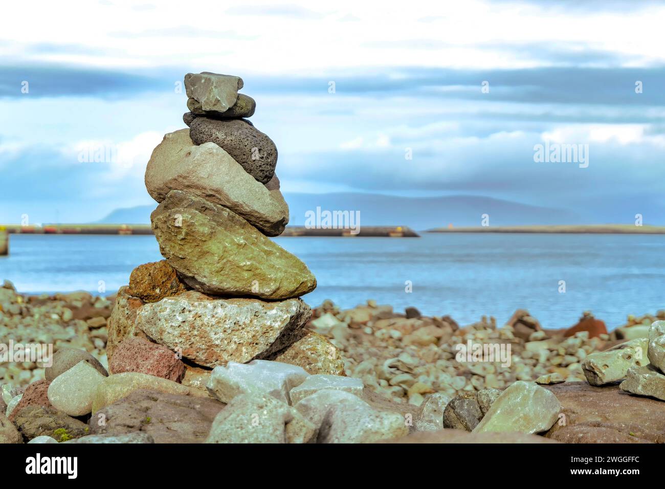 Opera creativa di bilanciamento di pietre grossolane, ruvide e irregolari di diversi colori, posizionate una sull'altra sul mare con terreno roccioso contro l'acqua Foto Stock