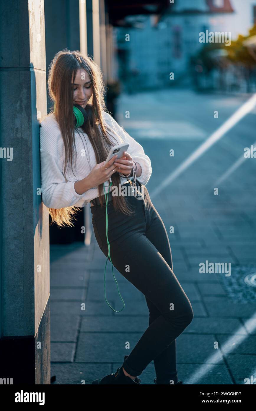 giovane donna in città al mattino presto navigando sui social network su uno smartphone Foto Stock