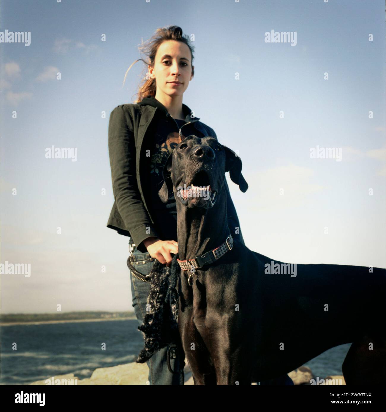 La giovane donna e il suo cane posano sulle rocce con l'oceano e l'isola sullo sfondo. Foto Stock