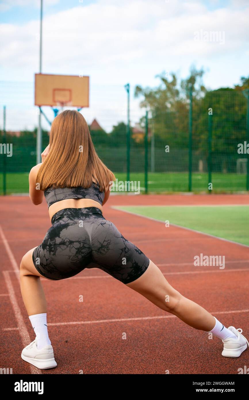 Foto di giovane donna sportiva accentrata in abbigliamento sportivo all'aperto in uno stadio che fa affondamento in esercizio Foto Stock