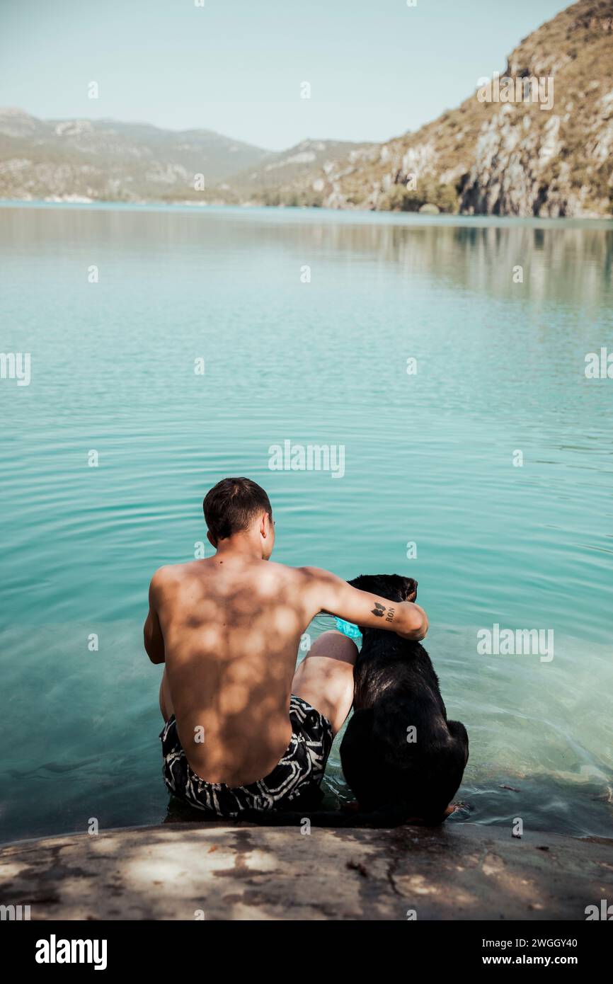 Ragazzo che abbraccia il suo cane in un lago con montagne sullo sfondo Foto Stock