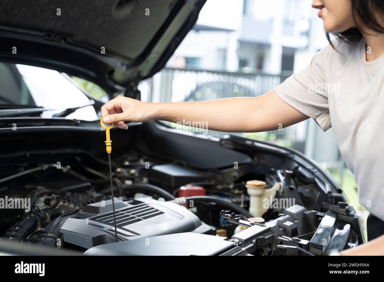 Donna in piedi accanto a un'auto con il cofano sollevato, a controllare il motore. Foto Stock