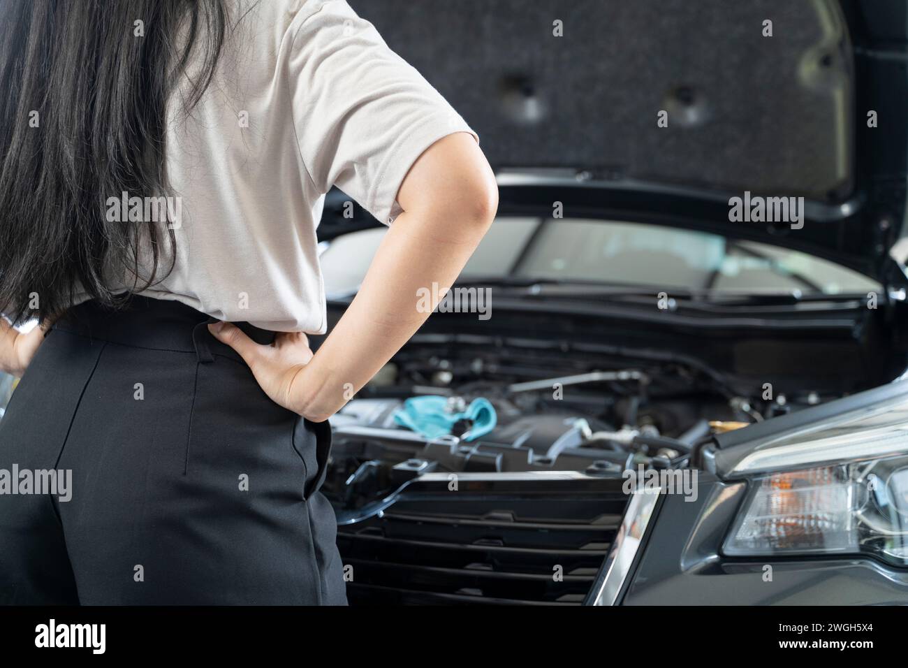 Donna asiatica che ha problemi con la sua auto bella donna che ispeziona la macchina rotta prima di uscire di casa. Foto Stock