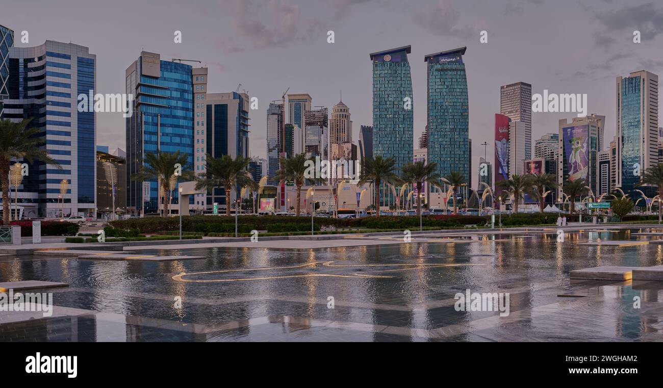 Skyline di Doha nella zona ovest della baia Doha, Qatar ripresa pomeridiana dal parco dell'hotel con lago artificiale in primo piano e nuvole in cielo sullo sfondo Foto Stock