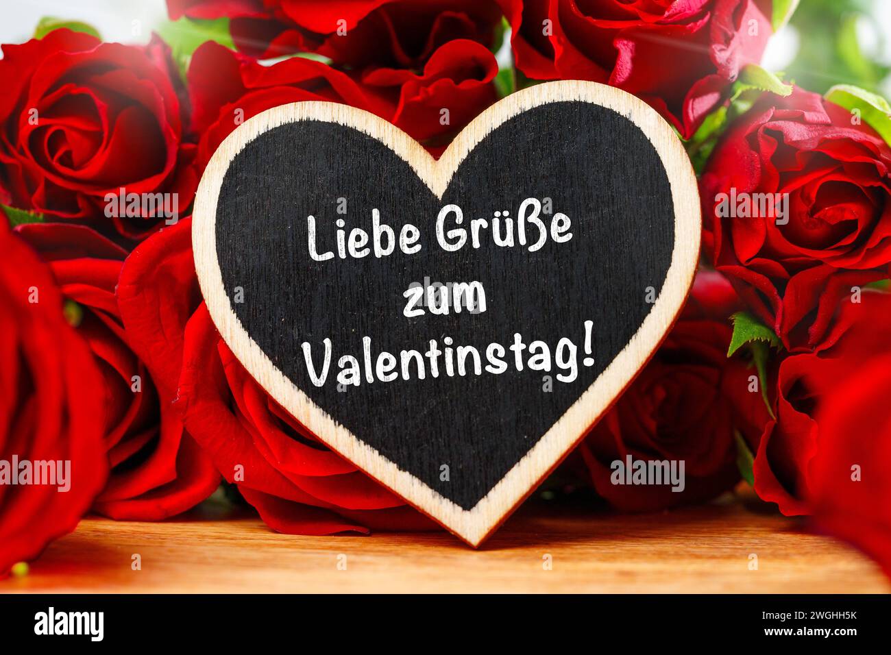 5 febbraio 2024: Saluti per la scritta di San Valentino su un cuore davanti alle rose rosse. FOTOMONTAGGIO *** Liebe Grüße zum Valentinstag Schriftzug auf einem Herz vor roten Rosen. FOTOMONTAGE Foto Stock