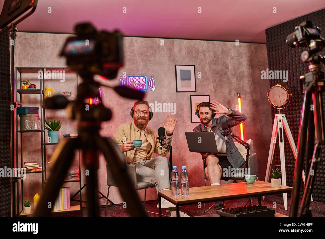 bell'uomo barbuto con le cuffie che bevono caffè e parlano durante il podcast, saltando le mani Foto Stock