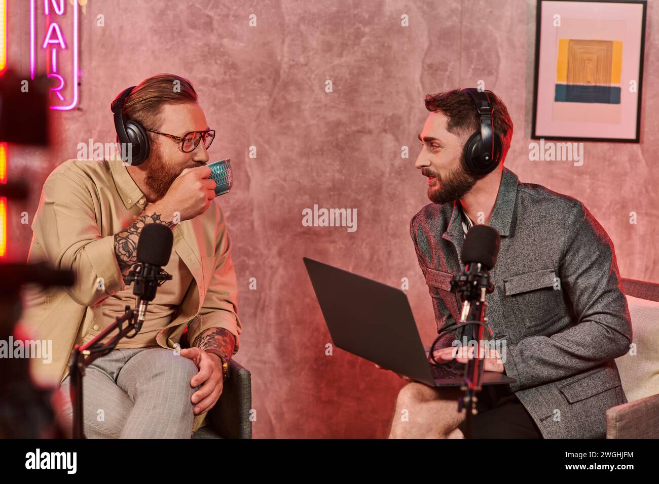 uomini con barba dall'aspetto accattivante con cuffie che bevono caffè e parlano attivamente durante il podcast Foto Stock
