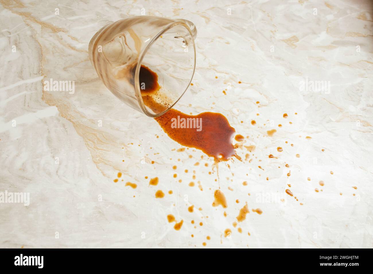Fuoriuscita di caffè da una tazza di vetro trasparente su fondo in marmo, messa a fuoco morbida in primo piano Foto Stock