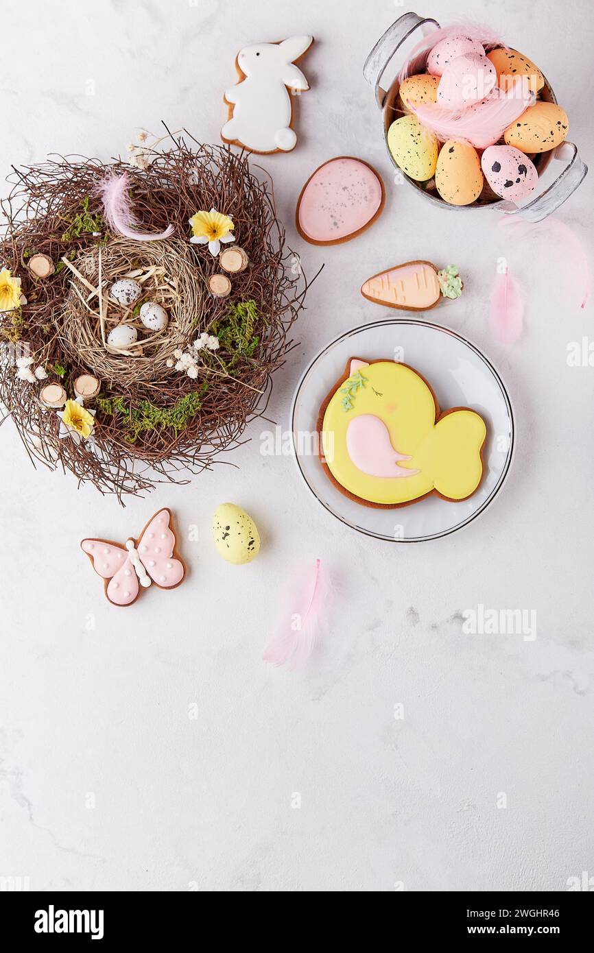 Estetica pasquale biscotti pastello smaltati, nido, decorazioni di piume sul tavolo, spazio copia. Foto Stock