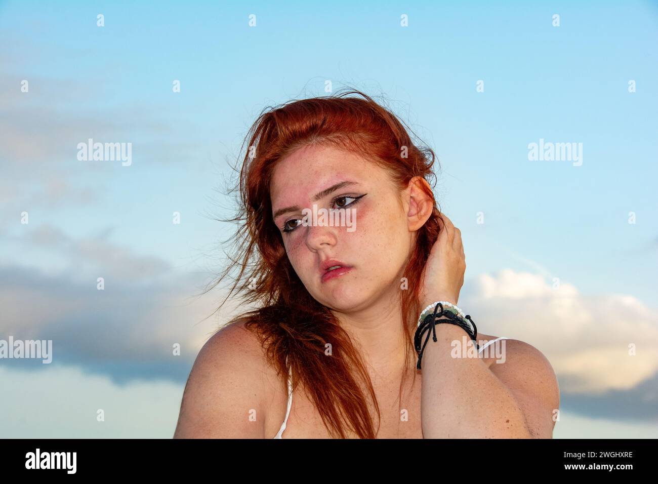 Ritratto di una giovane ragazza con i capelli rossi, il cielo blu e le nuvole, i capelli tormentati dal vento Foto Stock