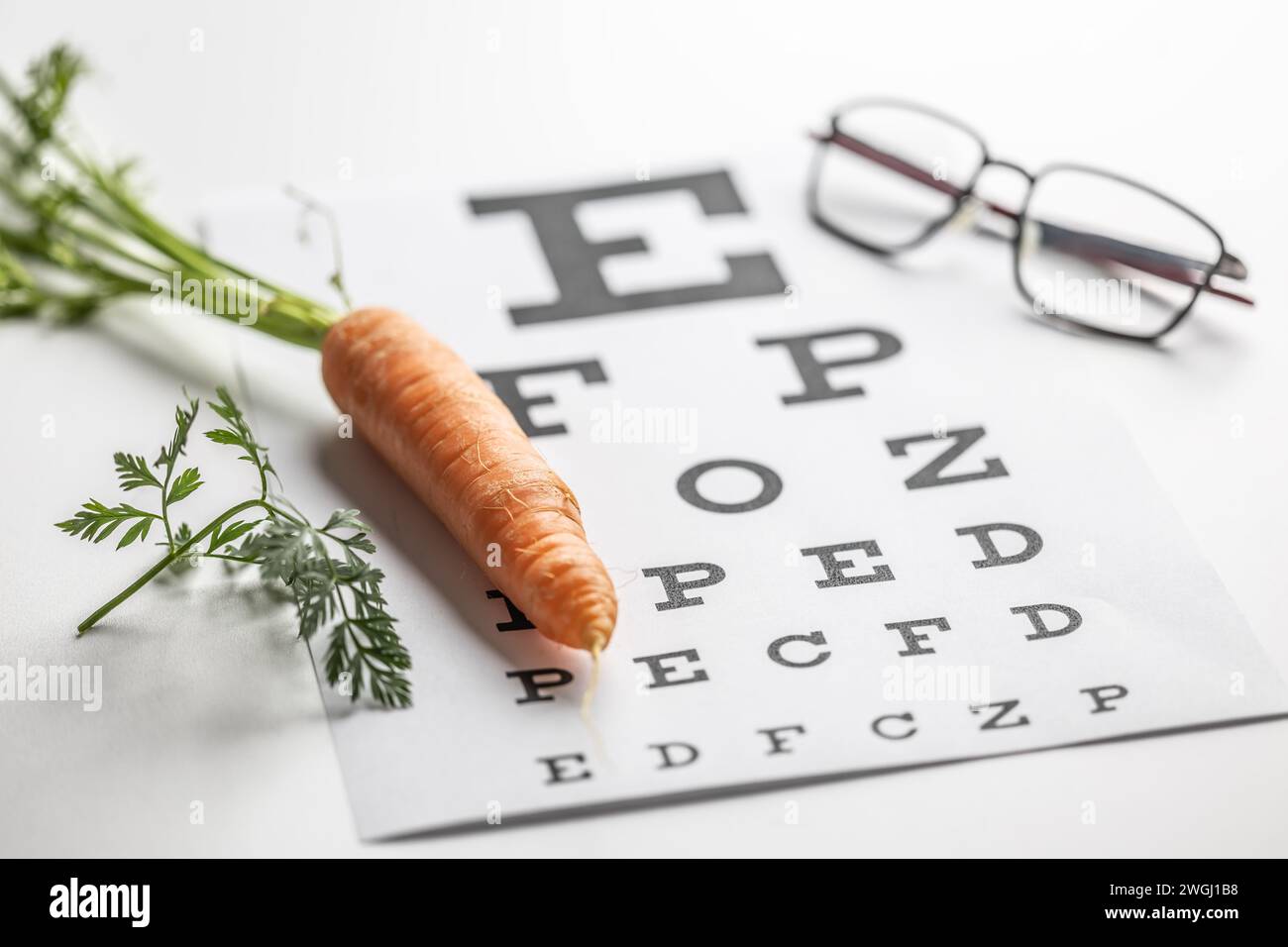 Carote fresche come fonte di vitamina A collocate sul grafico degli esami oculari. Bicchieri e carote, concetto di buona vista. Foto Stock