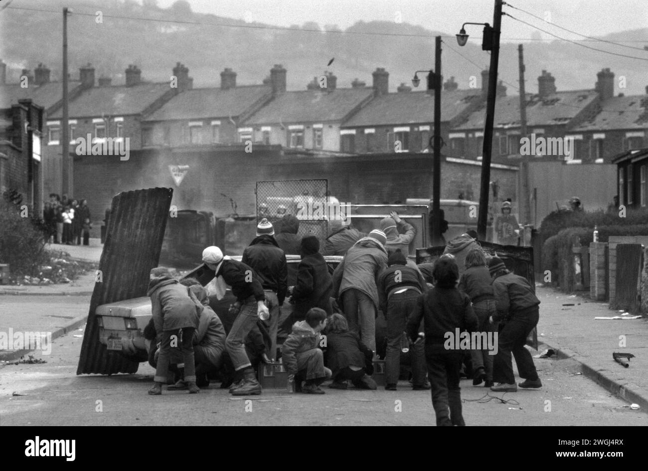 The Troubles Belfast Irlanda del Nord 1981. Auto dirottata incendiata da giovani giovani dell'IRA e usata come barricata nella lotta contro le bombe a benzina contro l'esercito britannico visto in background. 1980 anni Etna Drive, Ardoyne, nord di Belfast, Regno Unito, anni '1980, HOMER SYKES Foto Stock