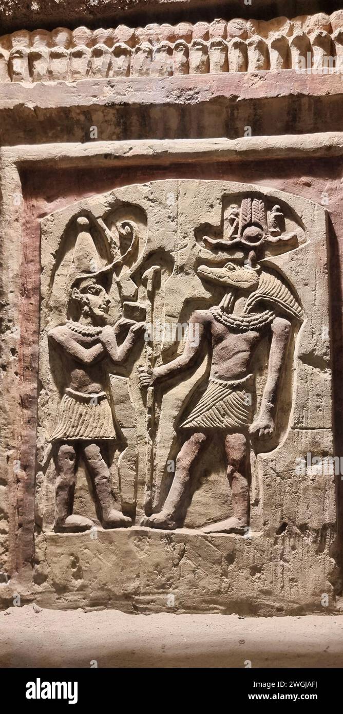 Un'antica opera d'arte egiziana adorna un vecchio edificio, che mostra simboli e figure accattivanti in mezzo a un raduno di persone Foto Stock