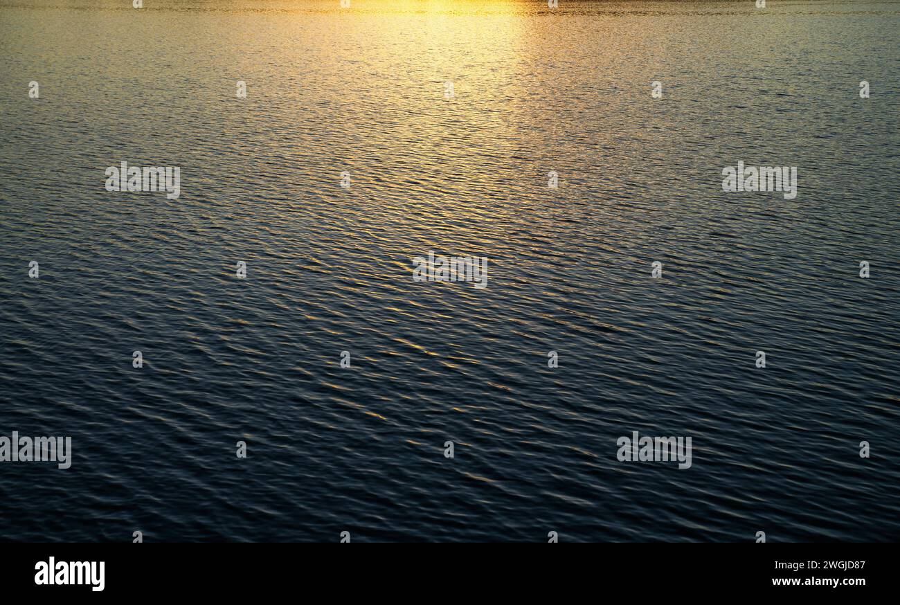 Superficie d'acqua con onde sotto i raggi del sole che tramonta. Foto Stock