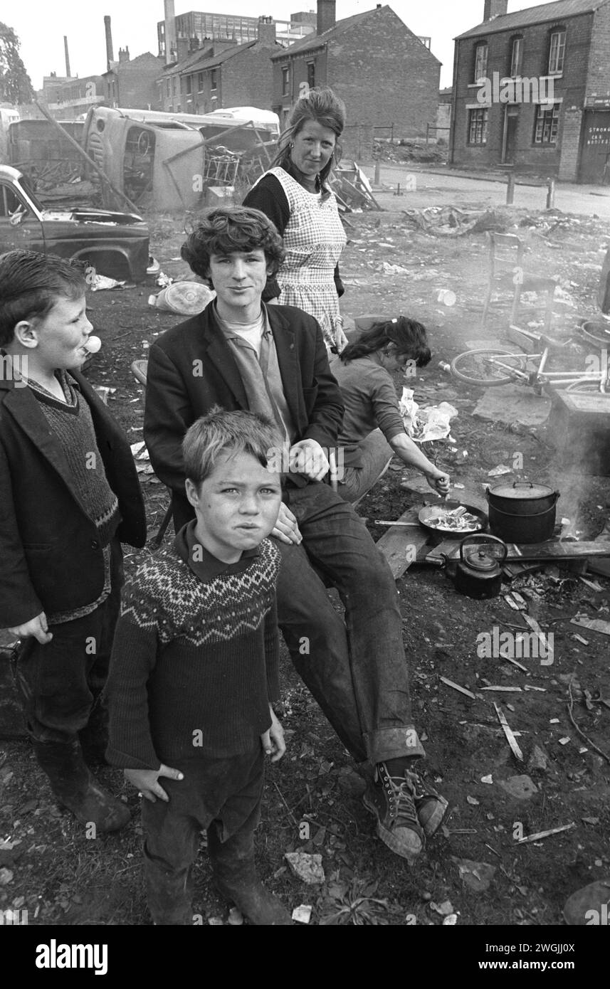 Gruppo familiare di viaggiatori irlandesi zingari, accampamento nel centro della città e scarico temporaneo di auto rottamate nel terreno di rifiuti di Balsall Heath. Un cuoco di famiglia, un pasto pomeridiano su un fuoco aperto. Le case sono su Emily Street. Balsall Heath, Birmingham, Inghilterra marzo 1968. 1960 UK HOMER SYKES Foto Stock