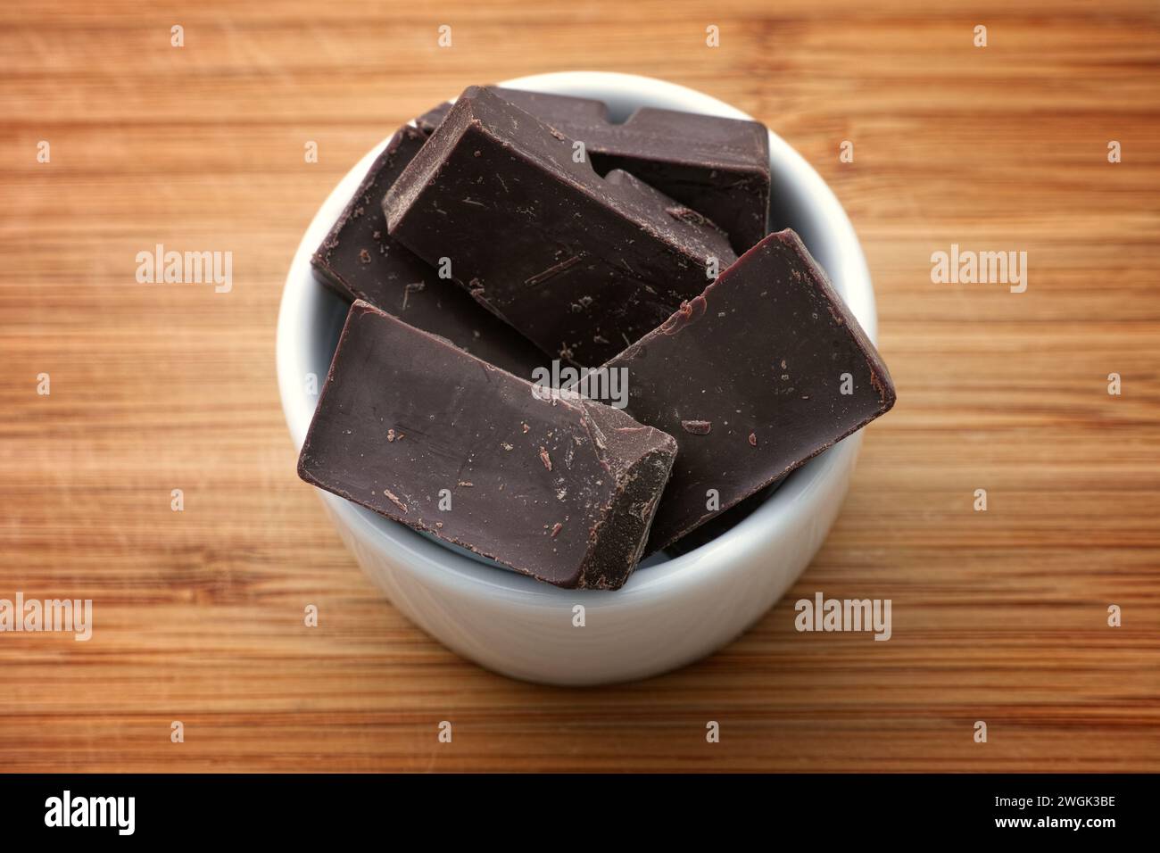 Pezzi di cioccolato fondente rotti in una piccola ciotola bianca. Primo piano. Foto Stock