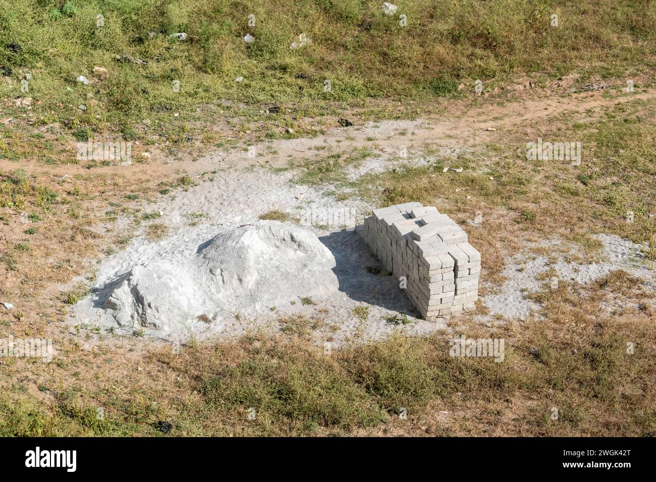 L'immagine mostra un mucchio di mattoni bianchi ben impilati accanto a un mucchio di calce sullo sfondo di un campo asciutto e erboso Foto Stock