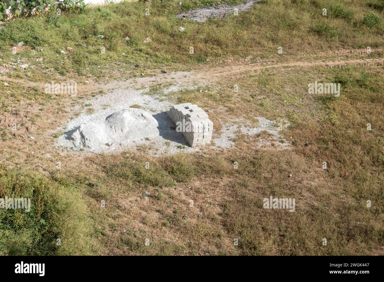 L'immagine mostra un mucchio di mattoni bianchi ben impilati accanto a un mucchio di calce sullo sfondo di un campo asciutto e erboso Foto Stock